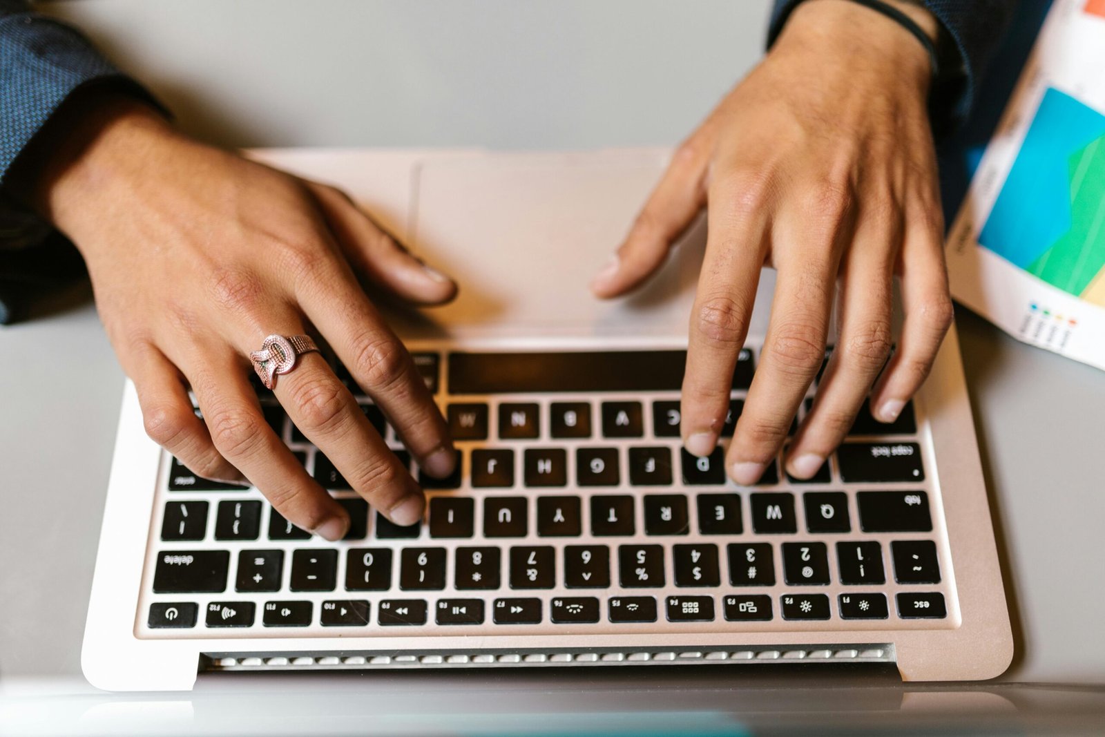 Hands typing on a laptop with a ring, emphasizing technology and work.