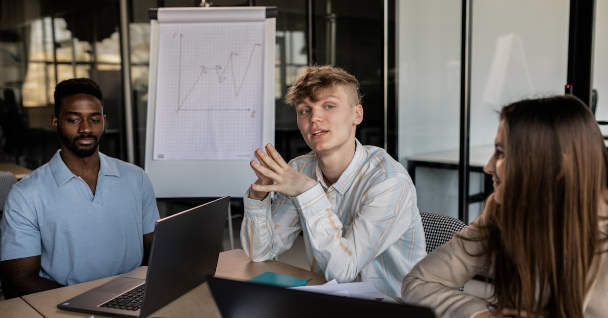 Three diverse colleagues engaged in a business strategy discussion in a modern office with a chart in the background.