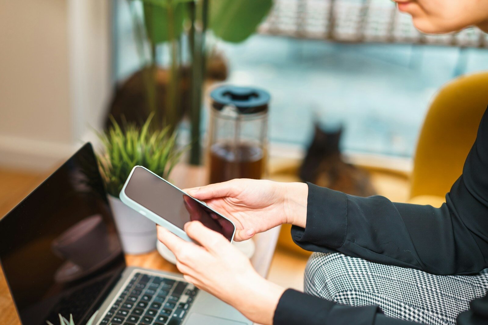 Person using a smartphone while working on a laptop