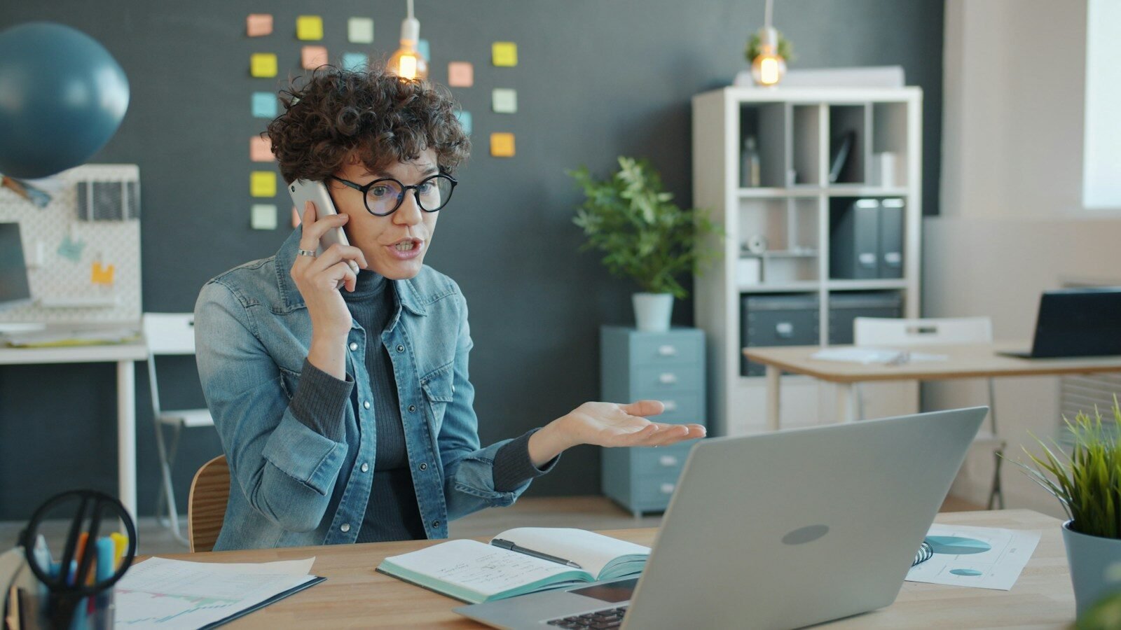 Woman talking on phone at desk with laptop